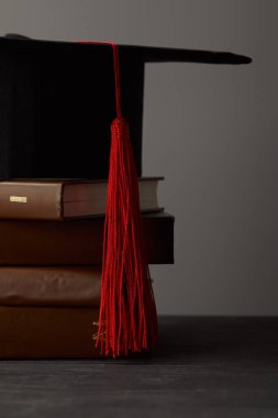 Gri üzerinde izole kırmızı püskül ile kahverengi kitaplar ve akademik kap