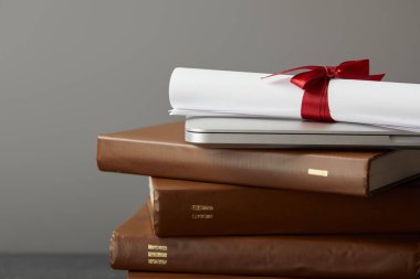 Kahverengi kitaplar, laptop ve kırmızı şerit ile diploma gri izole
