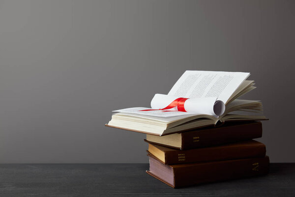 Books and diploma with red ribbon on dark surface on grey