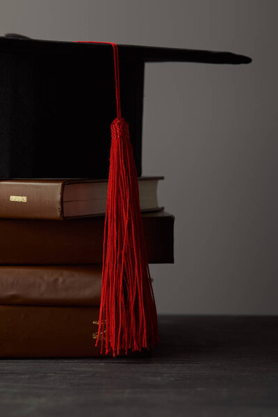 Коричневые книги и академическая шапка с красной кисточкой изолированы на сером
