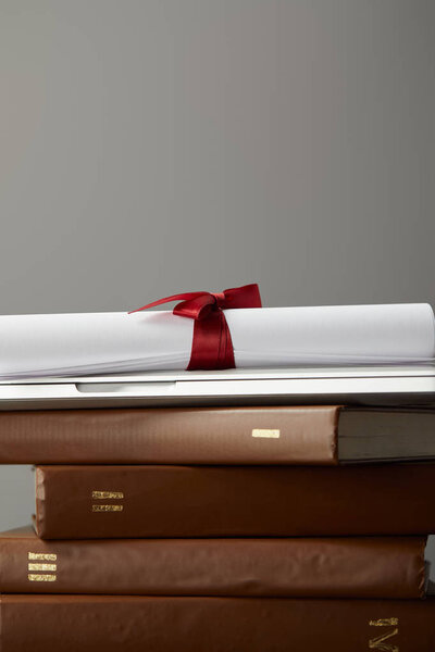 Brown books, laptop and diploma with red ribbon isolated on grey
