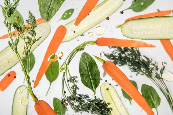 background with carrots, sliced cucumbers, spinach leaves, spices and water bubbles