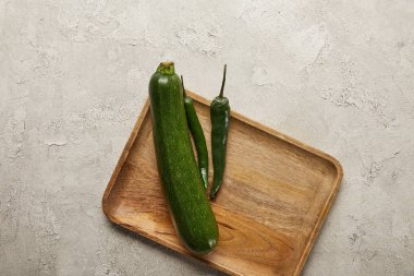 Top view of zucchini and chili peppers on wooden tray on textured surface clipart