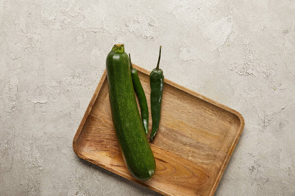 Top view of zucchini and chili peppers on wooden tray on textured surface