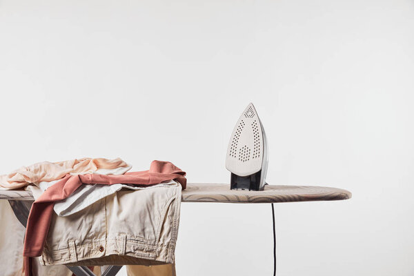 Clothes and iron on ironing board isolated on grey