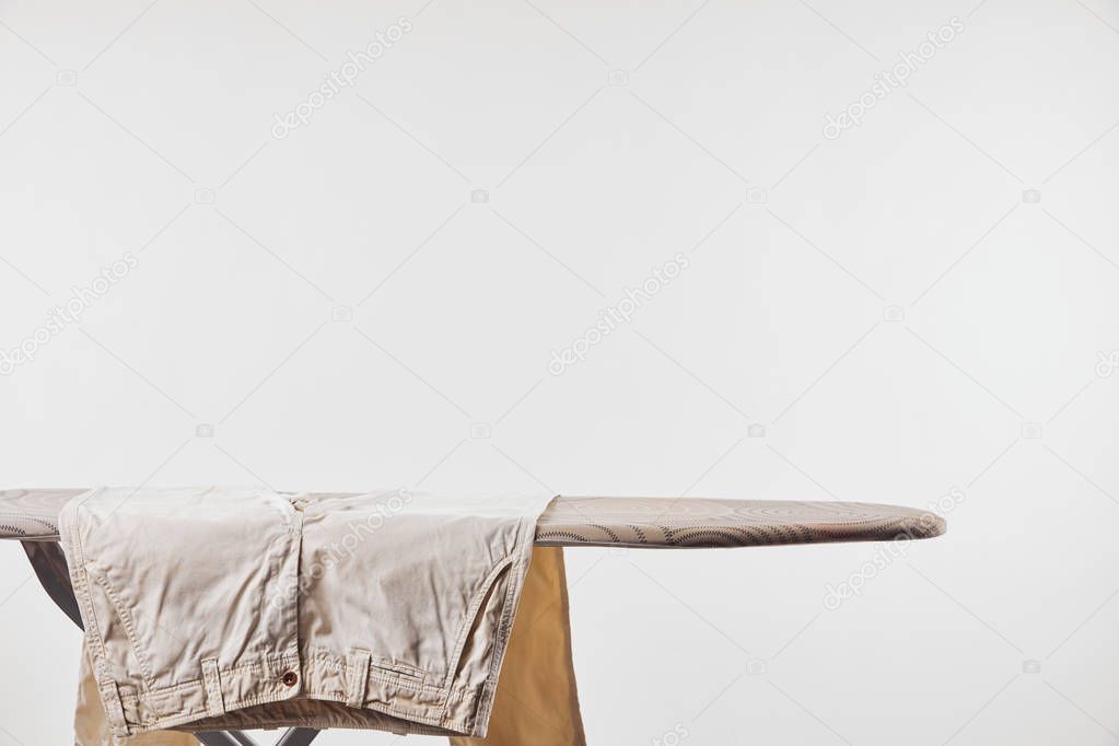 Beige male pants on ironing board isolated on grey