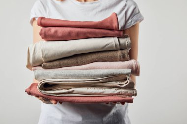 Cropped view of woman holding folded ironed clothes isolated on grey clipart