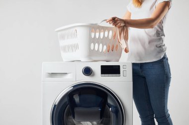 Gri üzerine izole edilmiş, Landry sepeti ve çamaşır makinesi olan kadınların kısmi görünümü