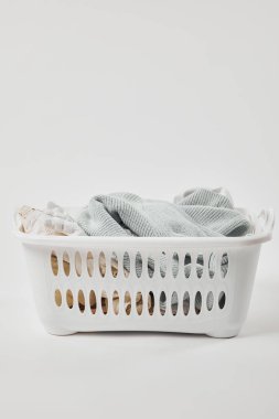 White plastic laundry basket with dirty clothes on grey clipart