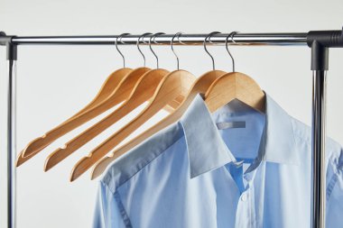 Straight rack, wooden hangers and blue shirt isolated on grey clipart
