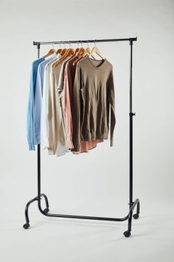 Straight rack, wooden hangers and male clothes isolated on grey clipart