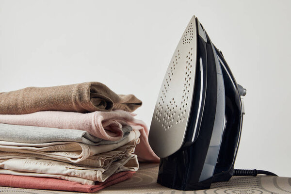 Iron and folded ironed clothes on ironing board isolated on grey