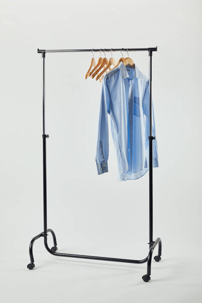 Прямая стойка, деревянные вешалки и голубая рубашка, изолированные на сером
