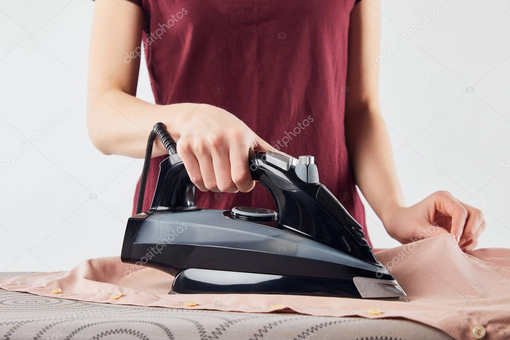 Cropped view of woman with black iron ironing shirt isolated on grey