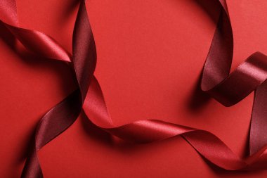 close up of curved silk burgundy and red ribbons on red background