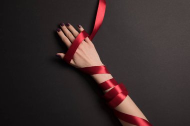 partial view of female hand with red ribbon on black background clipart
