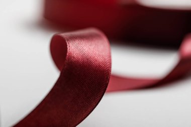 selective focus of shiny silk curved burgundy ribbon on grey background clipart