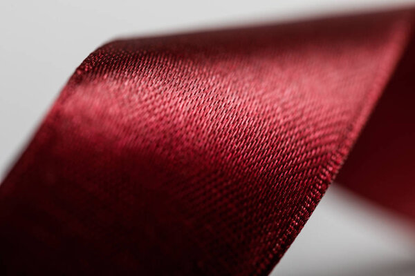 close up of shiny satin wavy burgundy ribbon on grey background