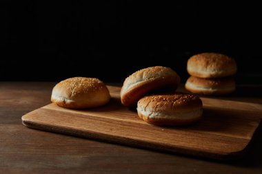 delicious buns with sesame on wooden chopping board isolated on black clipart