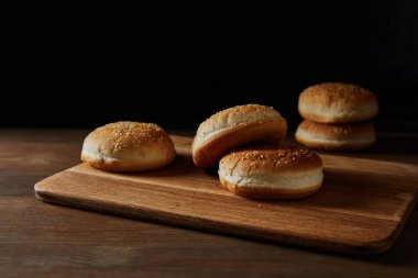 tasty buns with sesame on wooden chopping board isolated on black clipart