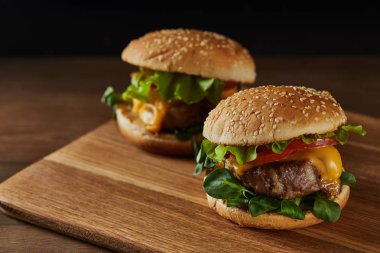tasty meat burgers with melted cheese on wooden chopping board