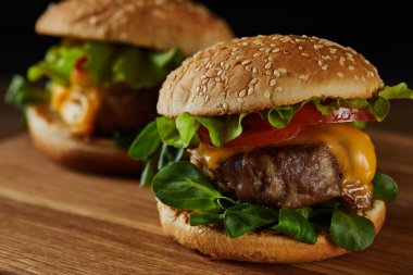selective focus of tasty meat burgers with cheese and greenery on wooden chopping board clipart