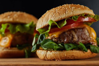 selective focus of delicious meat burgers with cheese and vegetables on wooden chopping board  clipart