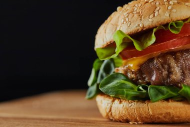 close up of delicious meat burger with cheese, greenery and sesame isolated on black clipart