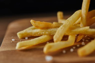 close up of fresh golden french fries with salt on wooden chopping board