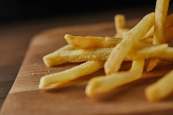 close up of fresh golden french fries on wooden chopping board