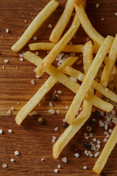top view of salt, black pepper and golden french fries on wooden chopping board