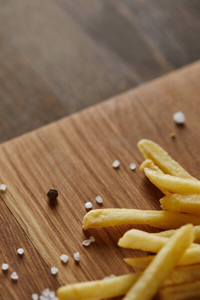 close up of tasty french fries with salt and black pepper on wooden chopping board