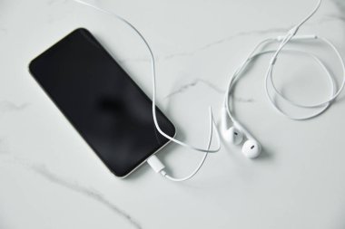 beyaz mermer yüzeyde boş ekran ve kablolu kulaklıklar ile akıllı telefonun üst görünümü
