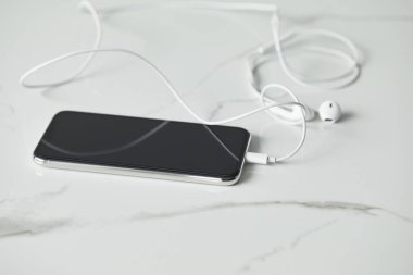 beyaz mermer yüzeyde bağlı kulaklıklar ile akıllı telefonun seçici odağı 