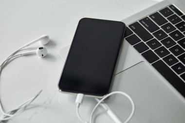 siyah klavyeli dizüstü bilgisayar, beyaz yüzeyde boş ekran ve kulaklıkları olan akıllı telefon