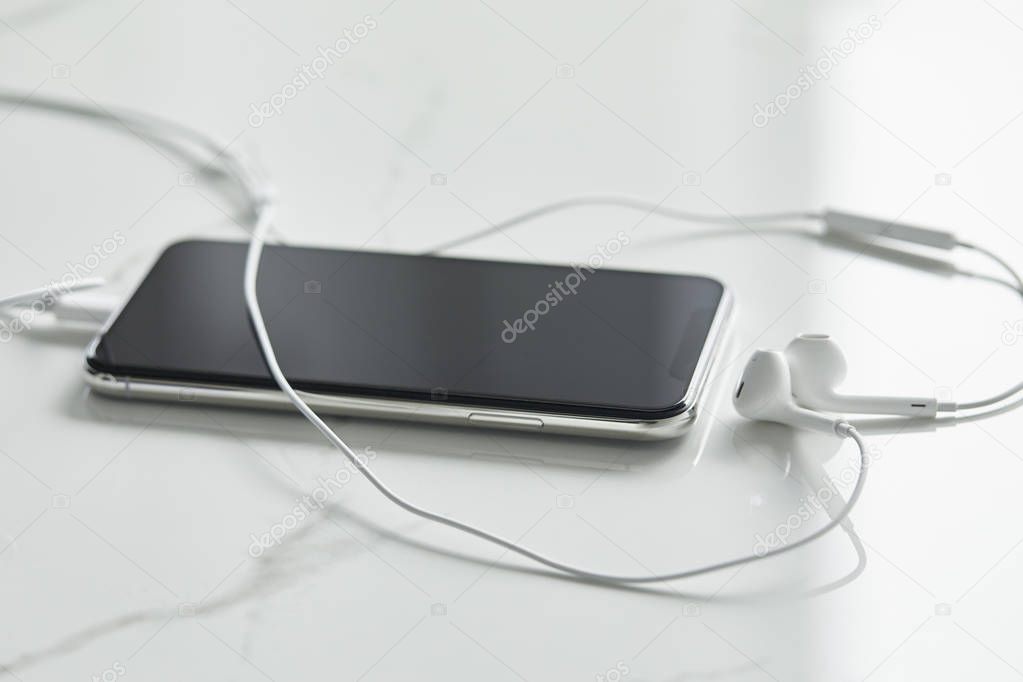 selective focus of smartphone with blank screen and wired earphones on white surface