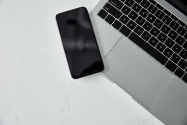 Beyaz yüzeyde siyah klavyeli boş ekran ve dizüstü bilgisayar ile akıllı telefonun üst görünümü