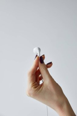 partial view of woman holding white earphone isolated on grey clipart