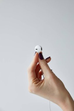cropped view of woman holding white wired earphone isolated on grey clipart