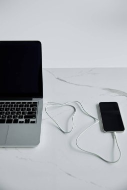 smartphone connected with cable to laptop with blank screen isolated on grey clipart