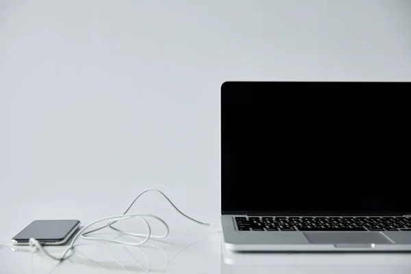 带空白屏幕的笔记本电脑和带连接耳机的智能手机隔离在灰色 — 图库照片