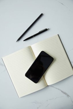 beyaz mermer yüzeyde boş ekran, Notebook, kalem ve kalem ile akıllı telefonun üst görünümü