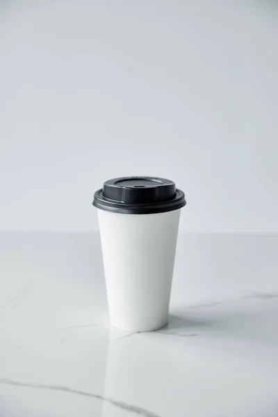 white disposable cup with black cap on white marble surface isolated on grey