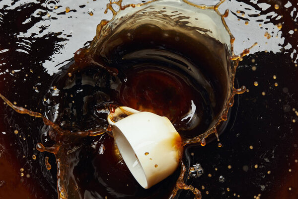 Overturned white porcelain cup with black coffee and splash