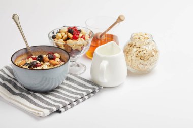 bowl on striped napkin with oat flakes, nuts and berries on white table with copy space clipart