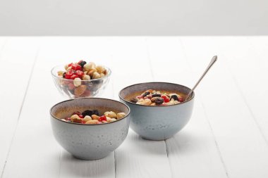 bowls with muesli, dried berries and nuts served for breakfast on white table isolated on grey clipart