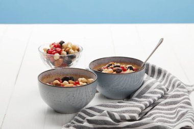 bowls with muesli, dried berries and nuts served for breakfast near striped napkin isolated on blue clipart