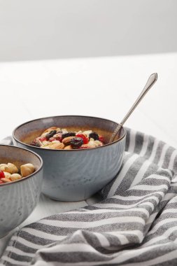 bowls with muesli, dried berries and nuts served for breakfast near striped cloth isolated on grey clipart
