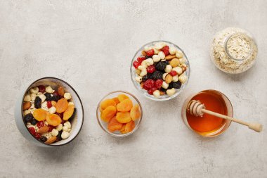 dokulu gri yüzeyde müsli, kurutulmuş kayısı ve çilek, fındık ve bal ile kase üst görünümü