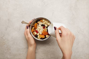 kadının sütten süt dökülme görünümü, müsli, kurutulmuş kayısı ve çilek, dokulu gri yüzeyde fındık ile kase içine